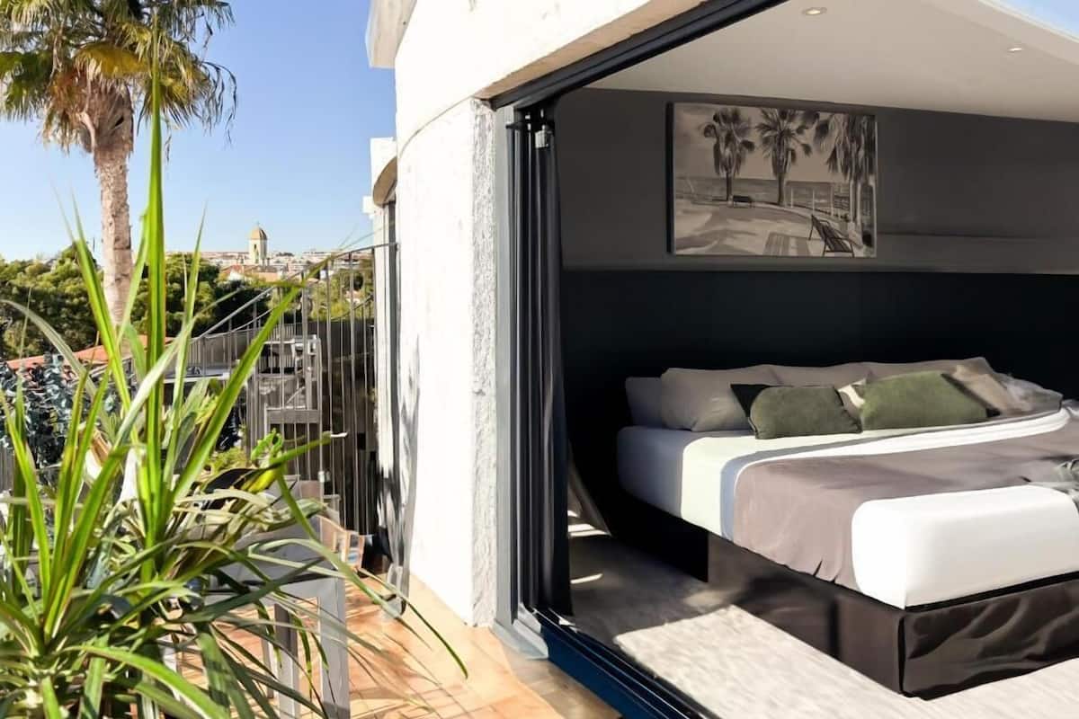 Un dormitorio moderno con cama, vistas a la ciudad y un balcón con plantas.