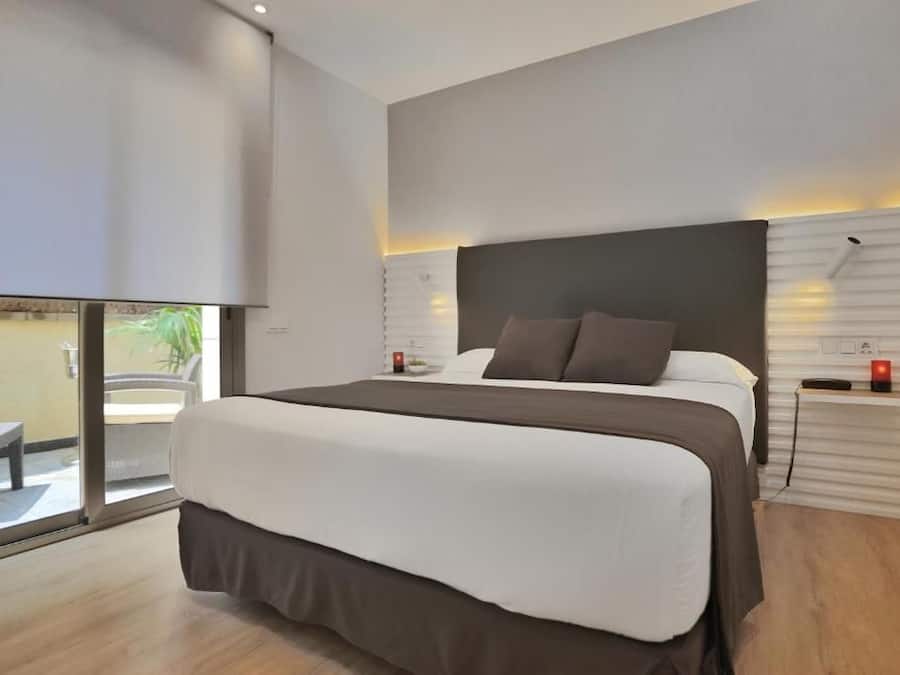 A modern hotel room with a large bed, a small table, and a view of the outdoors.