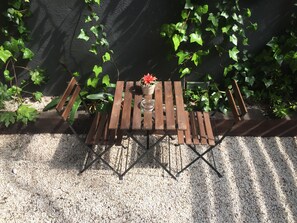 A wooden outdoor table with a vase and a red flower, surrounded by greenery and a gravel path. - Sitges (Sitges)