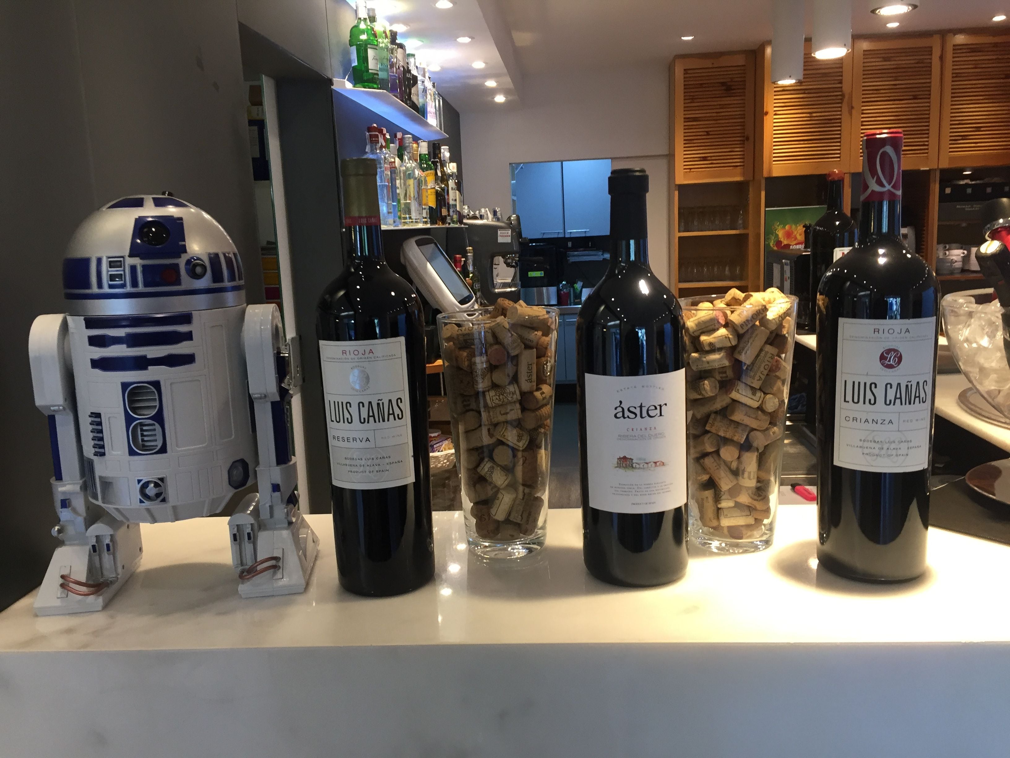 Una zona de bar con botellas de vino, una figurita de R2-D2 y una estantería para vinos.