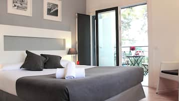 A modern hotel room with a large bed, a balcony with a table and chairs, and framed pictures on the wall.