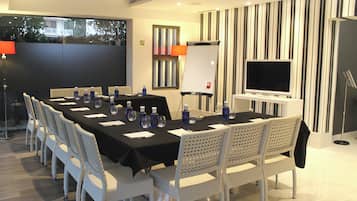 Un salón de conferencias con una larga mesa, sillas blancas, un televisor y una pizarra.