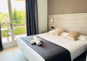 A hotel room with a large bed, a nightstand, a wall-mounted lamp, and a view of the outdoors through a sliding door. - Sitges (Sitges)