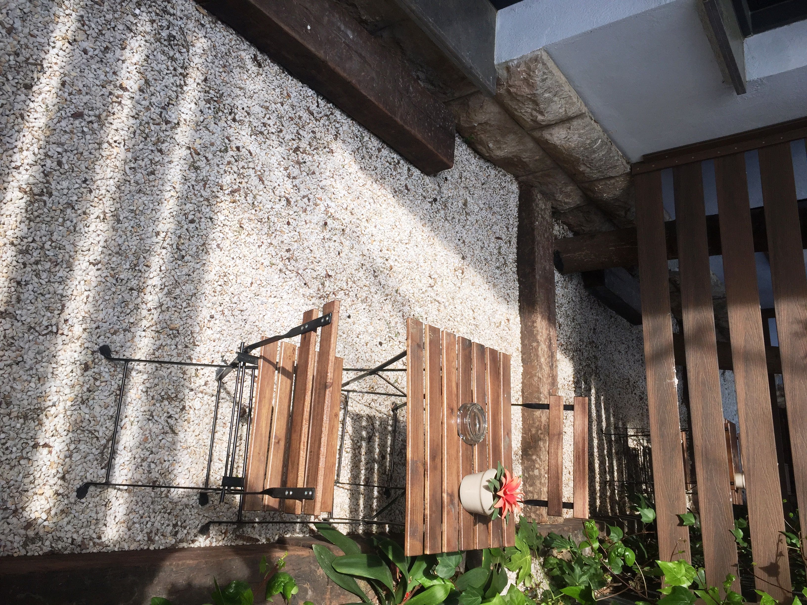 Un espacio al aire libre rústico con cerca de madera, portón de metal y pared de piedra.