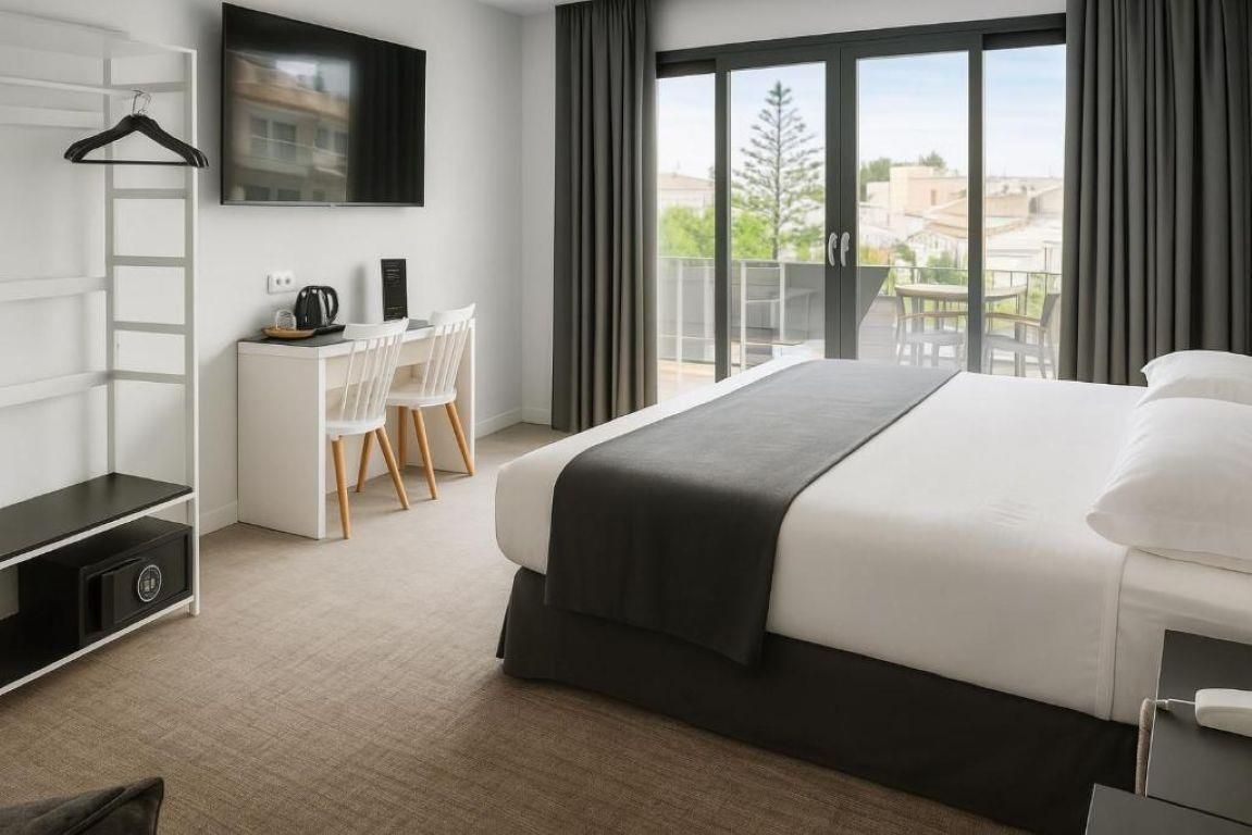 A modern hotel room with a large bed, a desk with a chair, a TV mounted on the wall, and a balcony with a view of the city.