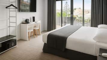 A modern hotel room with a large bed, a desk with a chair, a TV mounted on the wall, and a balcony with a view of the city.