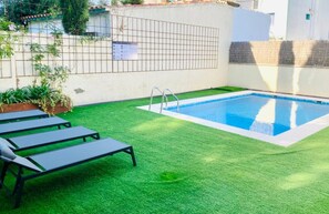A swimming pool with a metal ladder, surrounded by artificial grass and a metal fence. - Sitges (Sitges)