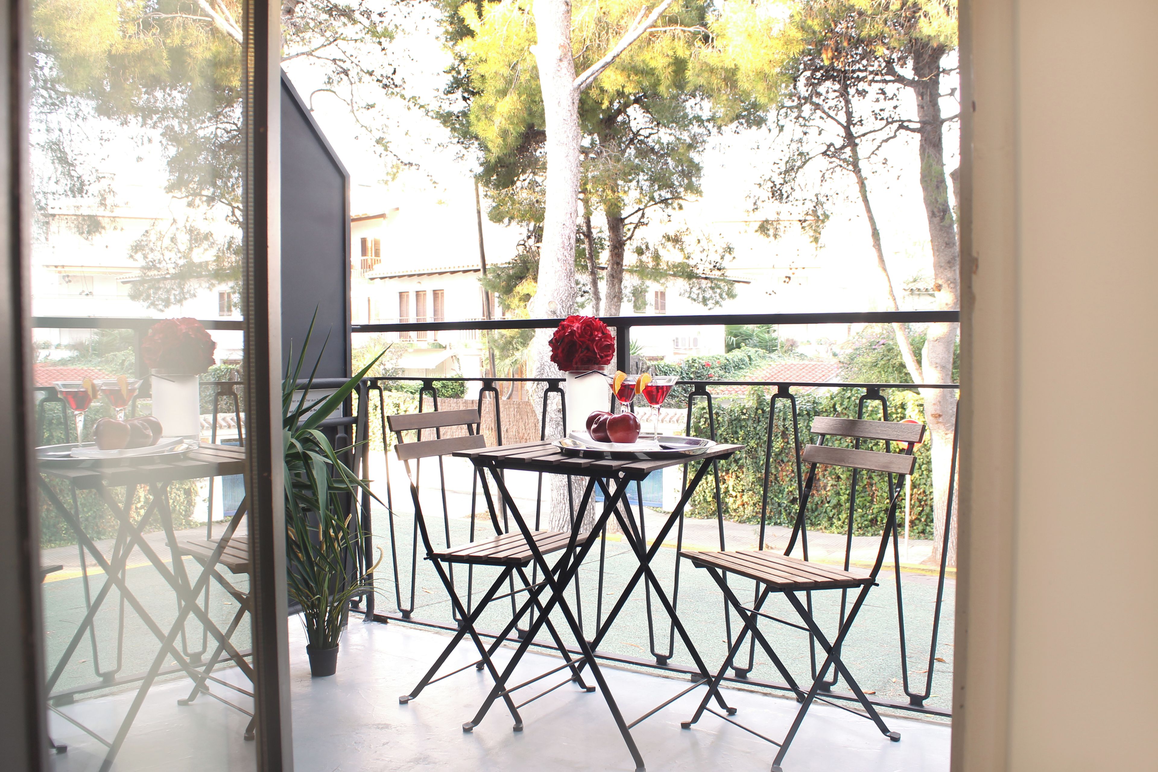 Un balcon avec une table et des chaises, un pot de fleurs et une vue sur les arbres et les bâtiments.