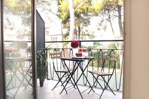 Un balcón con una mesa y sillas, una planta en maceta y vistas a árboles y edificios.