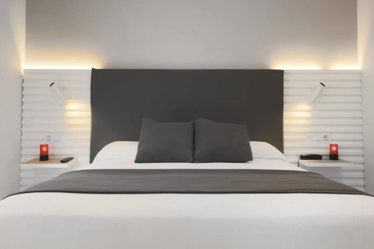 Un dormitorio moderno con una cama grande, dos mesitas de noche e iluminación en la pared.