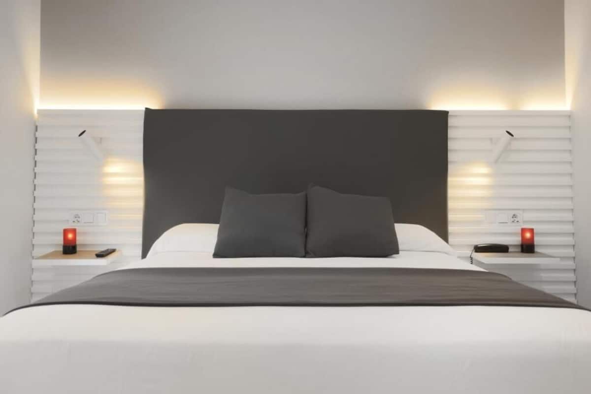 A modern bedroom with a large bed, two bedside tables, and wall-mounted lighting.
