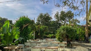 An outdoor patio with tables and chairs, surrounded by lush greenery and trees. - Sitges (Sitges)