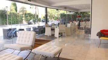 A modern indoor seating area with cushioned chairs and tables, large windows offering a view of the outdoors.