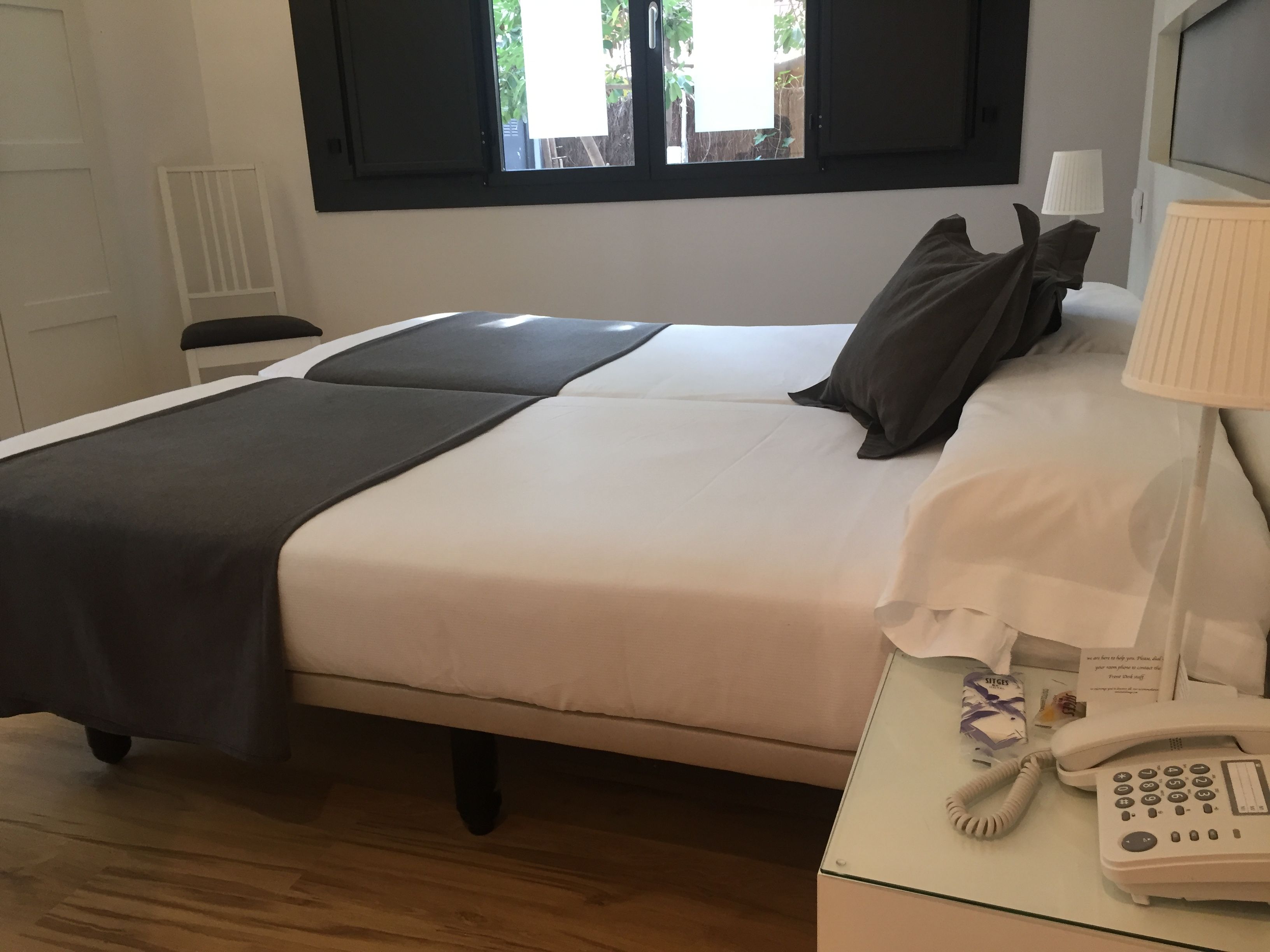 Une chambre d’hôtel avec un lit, une table de chevet avec une lampe et un téléphone, une fenêtre donnant sur un espace verdoyant et une porte.