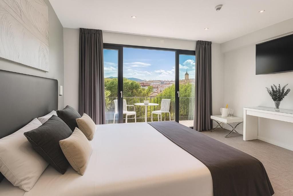 Una habitación de hotel moderna con una cama grande, un escritorio y un balcón con vistas a la ciudad.