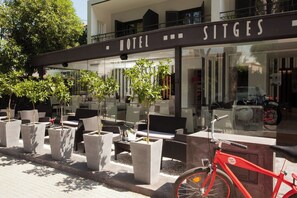 A hotel exterior with outdoor seating, potted plants, and a red bicycle. - Sitges (Sitges)