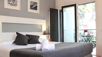 A modern hotel room with a large bed, a nightstand, a lamp, and a balcony with a table and chairs.