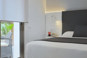 A modern hotel room with a large bed, a bedside table with a red candle, and a view of the outdoor balcony. - Sitges (Sitges)