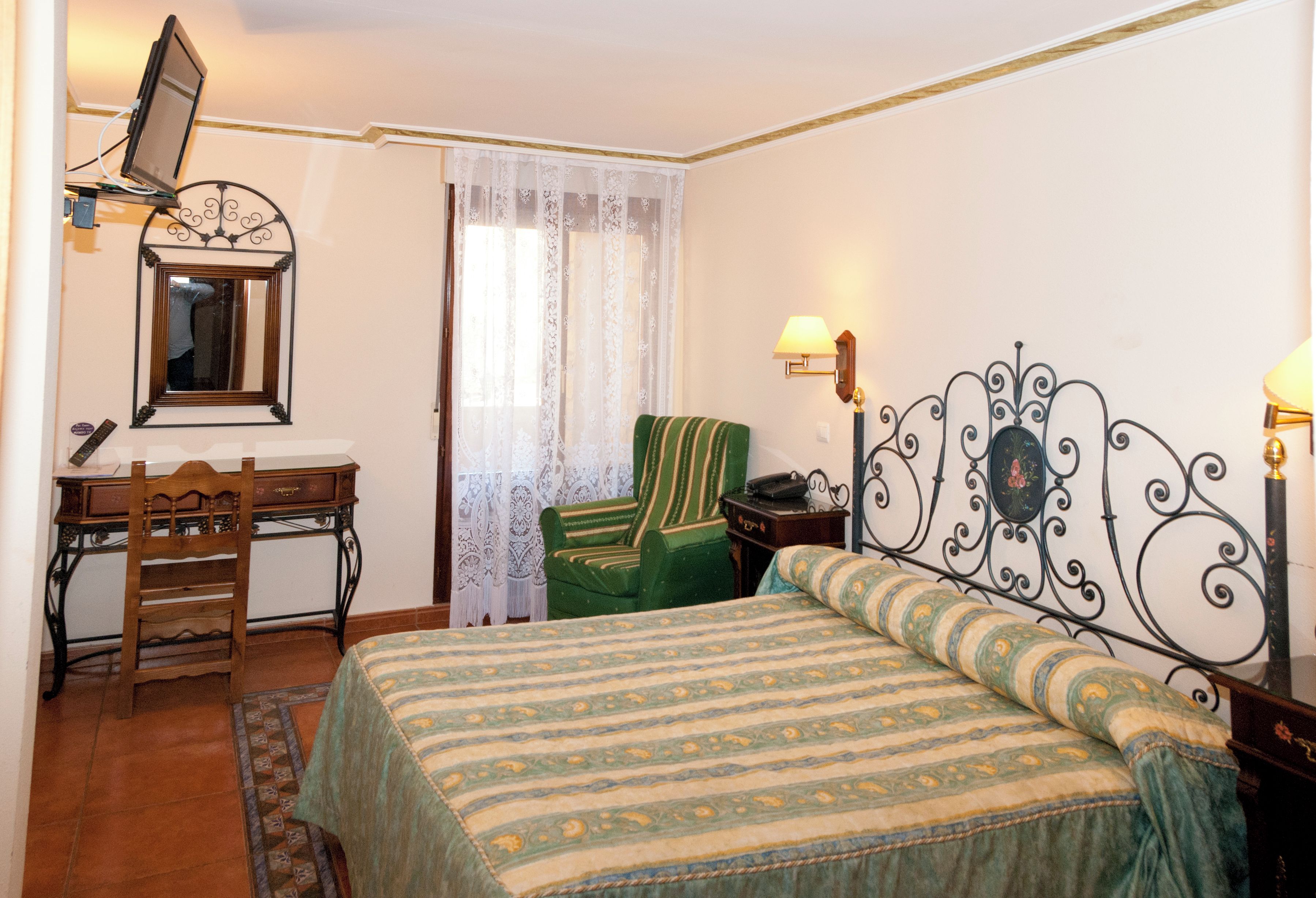 Un dormitorio con cama, escritorio, silla, espejo y ventana con cortinas.