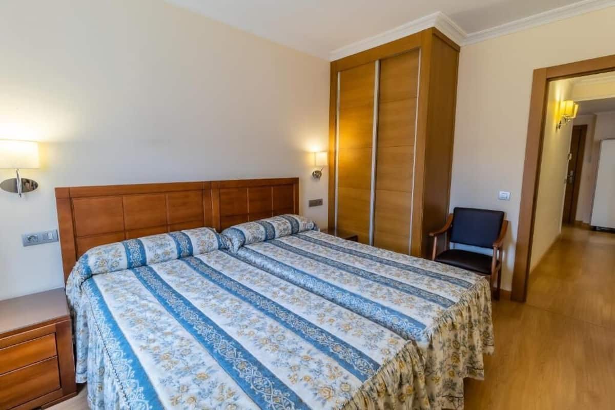 A bedroom with a large bed, wooden headboard, and a nightstand. There is a chair and a lamp in the corner.