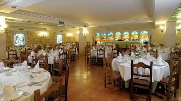 Un salón de banquetes con varias mesas redondas dispuestas para cenar, cada una con mantel blanco y cubertería.