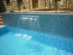 A swimming pool with a waterfall feature, surrounded by a stone wall and a metal fence. - Santo Domingo De Silos (Santo Domingo de Silos)