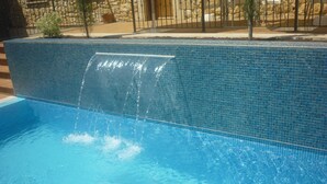 Piscina con cascata, circondata da un muro in pietra e un recinto in metallo.