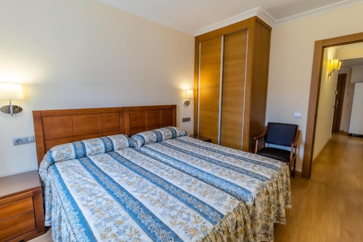 A bedroom with a large bed, wooden headboard, and a nightstand. There is a chair and a lamp in the corner.