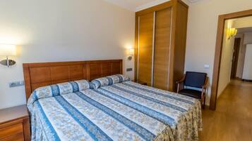 Un dormitorio con una cama grande, cabecera de madera y una mesita de noche. Hay una silla y una lámpara en la esquina.
