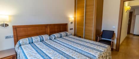 Een slaapkamer met een groot bed, houten hoofdbord en nachtkastje. Er staat een stoel en een lamp in de hoek.