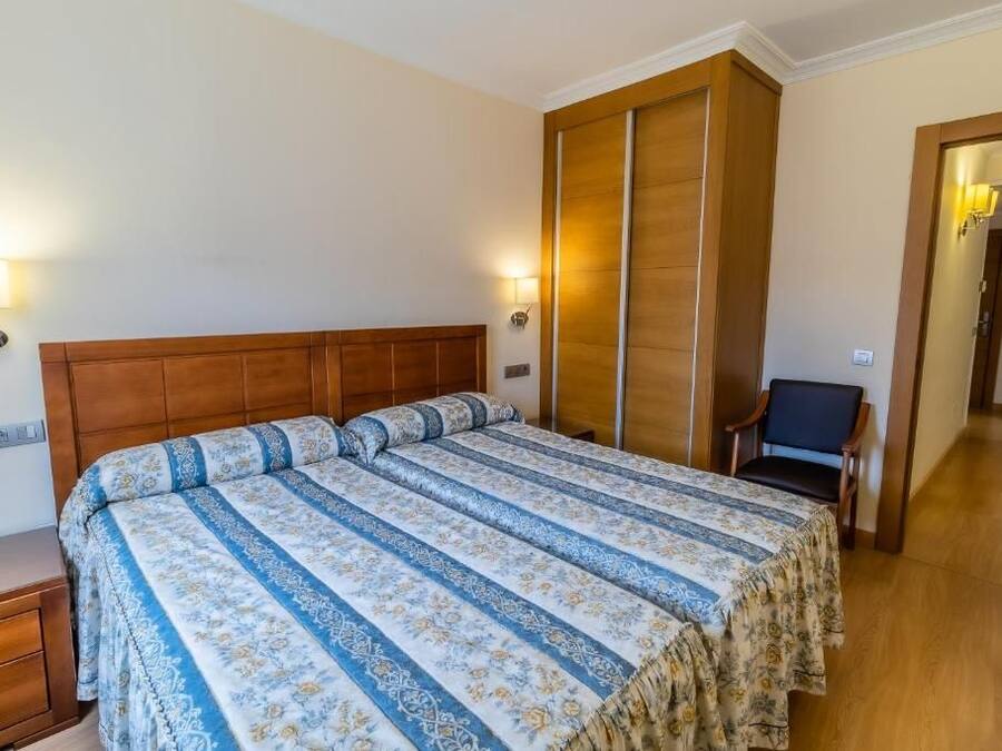 A bedroom with a large bed, wooden headboard, and a nightstand. There is a chair and a lamp in the corner.