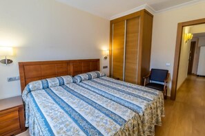 A bedroom with a large bed, wooden headboard, and a nightstand. There is a chair and a lamp in the corner. - Santo Domingo De Silos (Santo Domingo de Silos)