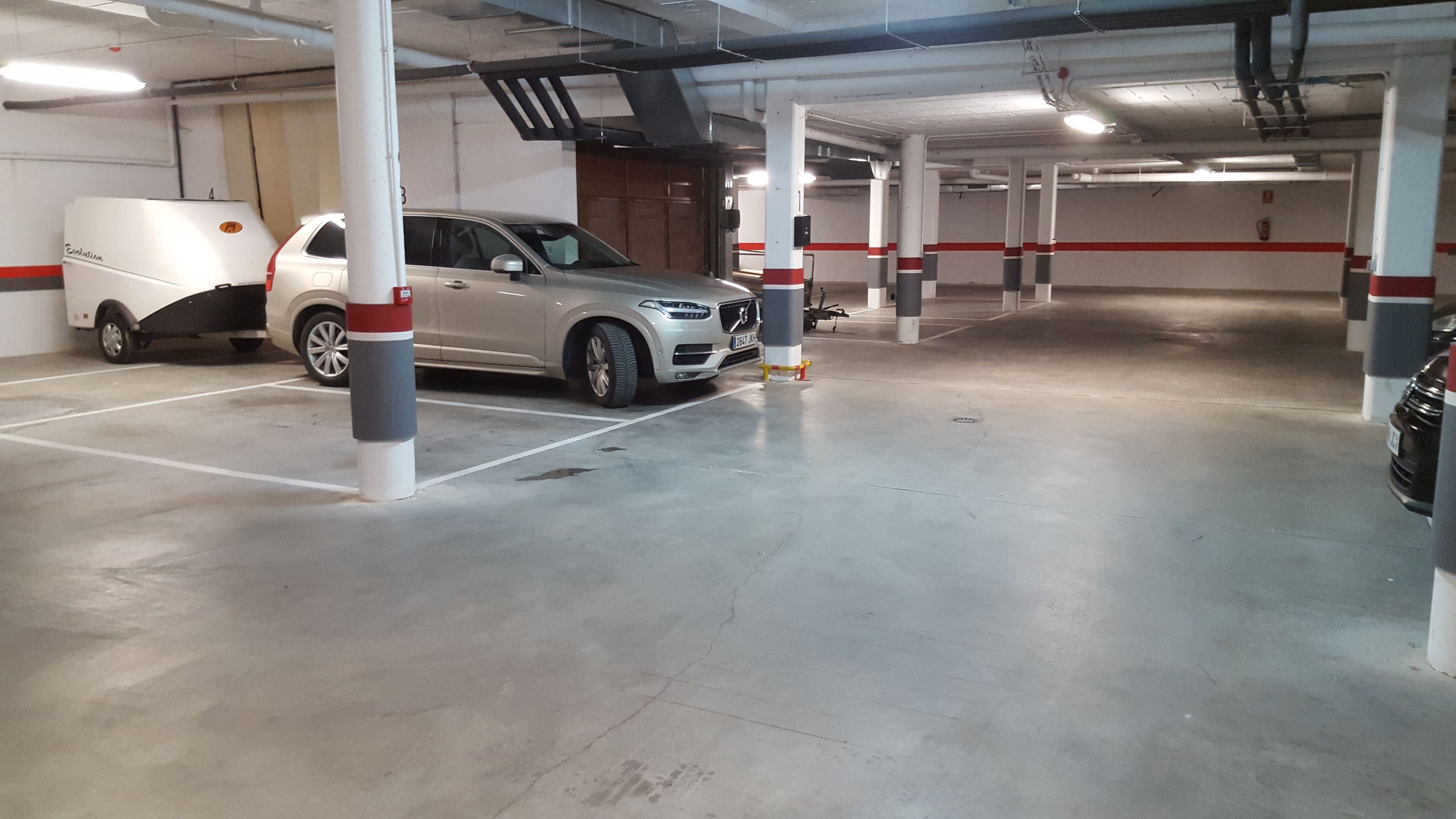 Autotalli, jossa on betonilattia, valkoiset pylväät, joissa on punaisia raitoja, ja hopeanvärinen maasturi on pysäköity sille varattuun paikkaan.