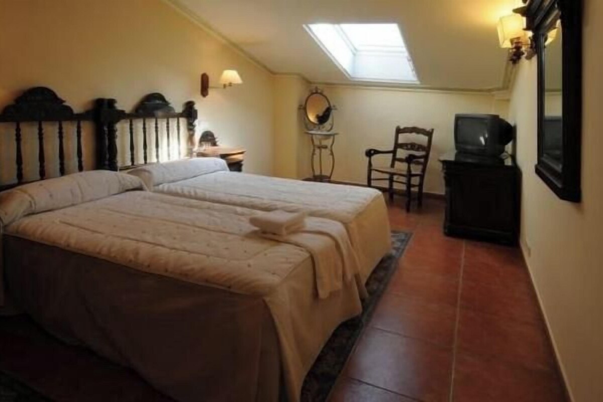 A bedroom with two beds, a desk, a chair, a television, and a skylight.