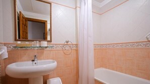 Egy fürdőszoba, amelyben mosdókagyló, WC, fürdőkád és zuhanyfüggöny található.