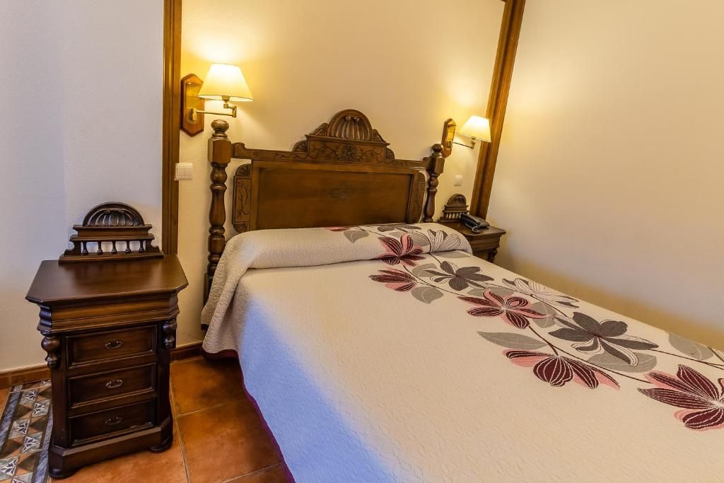 Un dormitorio con una cama de madera, dos lámparas de noche, una mesita de noche con cajones y una colcha estampada.