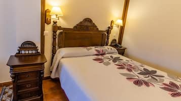Un dormitorio con una cama de madera, dos lámparas de noche, una mesita de noche con cajones y una colcha estampada.