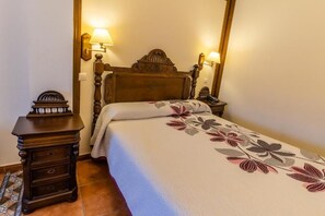 A bedroom with a wooden bed, two bedside lamps, a nightstand with drawers, and a patterned bedspread. - Santo Domingo De Silos (Santo Domingo de Silos)