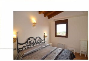 A bedroom with a bed, a nightstand, a dresser, a window with a view, and a wall-mounted light fixture. - Santo Domingo De Silos (Santo Domingo de Silos)