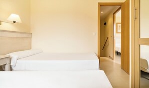 A hotel room with two beds, a bedside table, a lamp, and a wooden door. - Ilunion Sancti Petri (Chiclana de la Frontera)