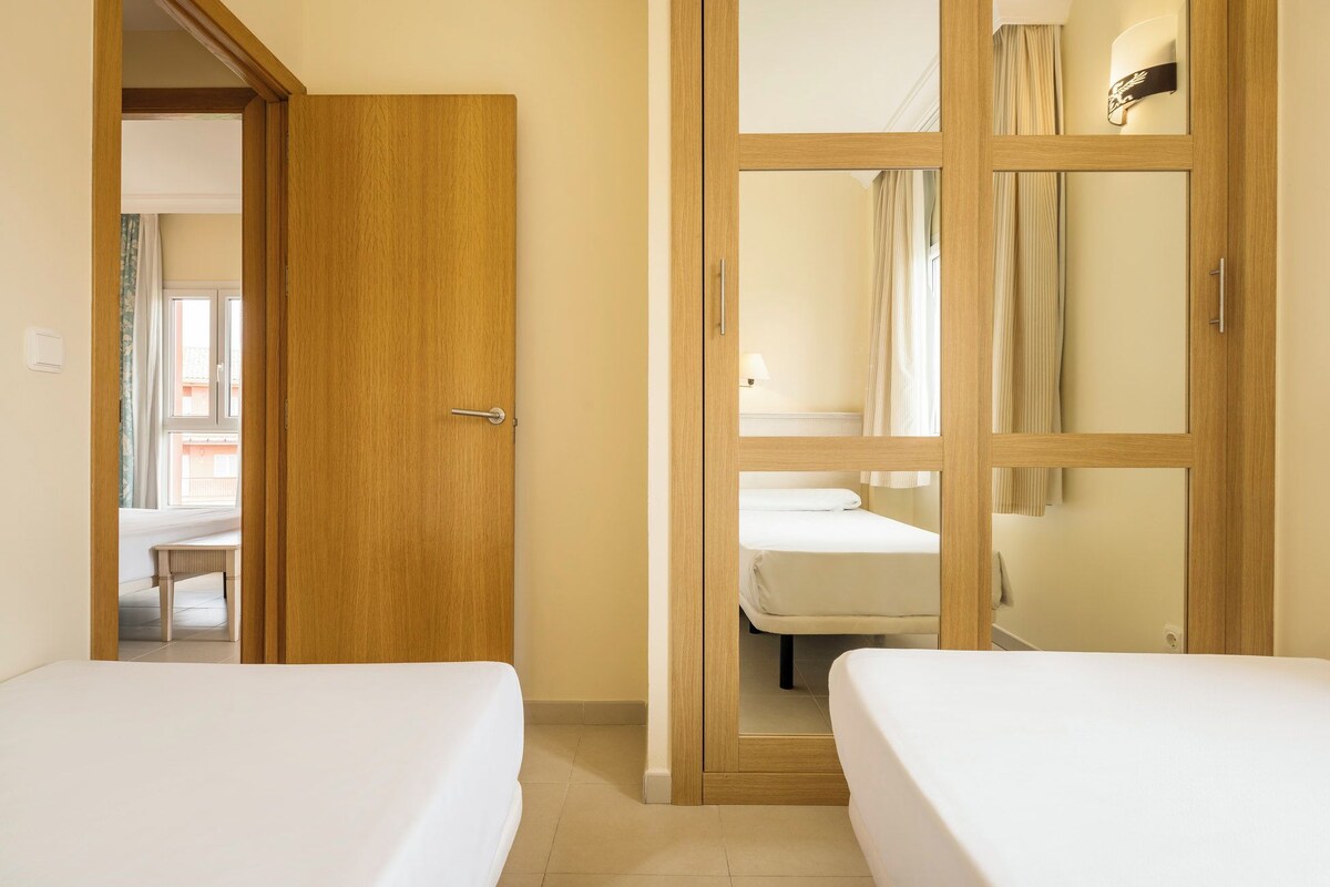 Ein Hotelzimmer mit zwei Betten, einem Holzschrank und einem durch eine Glastür einsehbaren Badezimmer.