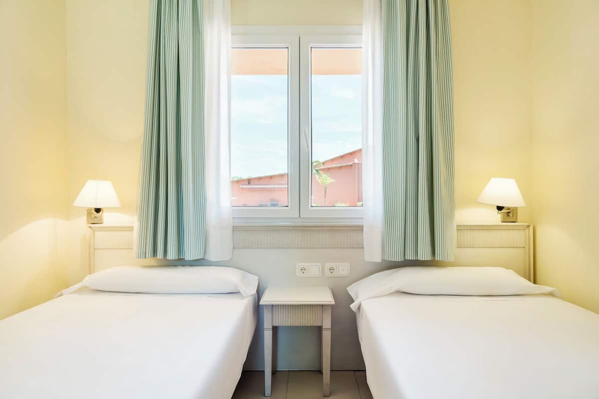 Habitación de hotel con dos camas, una mesita pequeña y una ventana con cortinas.