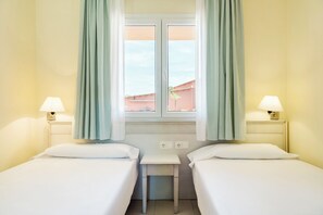 A hotel room with two single beds, a small table, two bedside lamps, and a window with curtains. - Ilunion Sancti Petri (Chiclana de la Frontera)