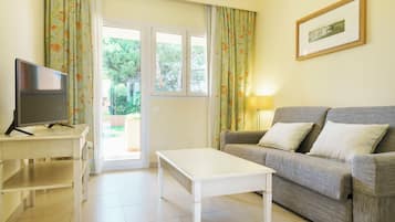 Una sala de estar con un sofá, un televisor sobre un mueble, una mesa y una puerta que da al exterior.