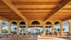 L’entrée d’un hôtel avec un plafond en bois, des fenêtres en arc de cercle et des plantes en pot.
