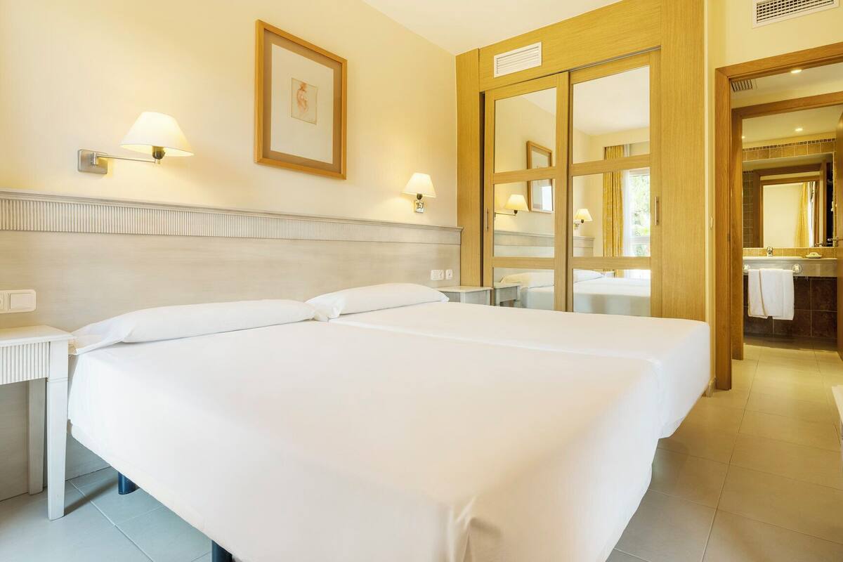 A hotel room with two beds, a bathroom with a mirror, and a small table.
