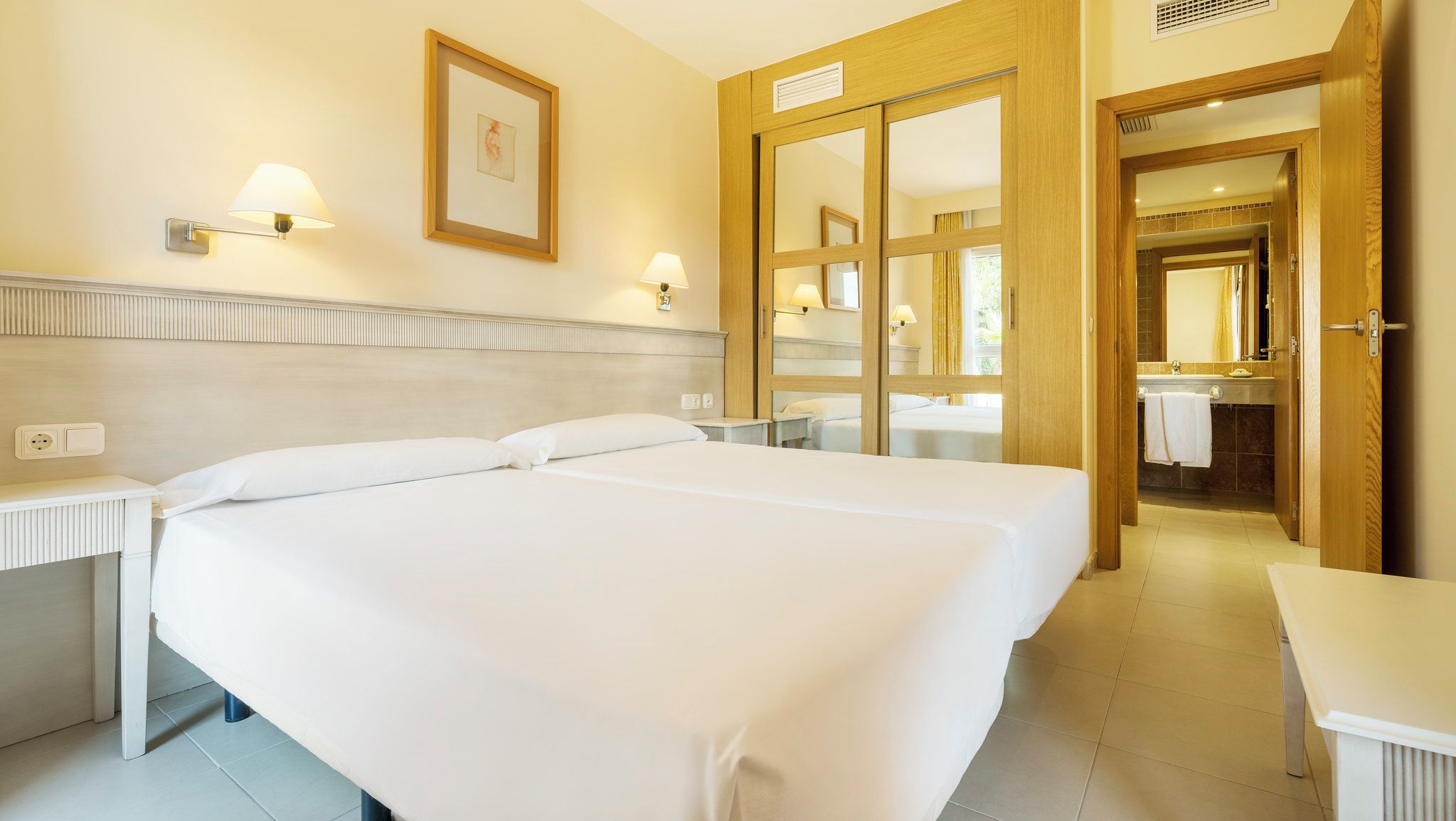 Habitación de hotel con dos camas, un baño con espejo y una mesita.