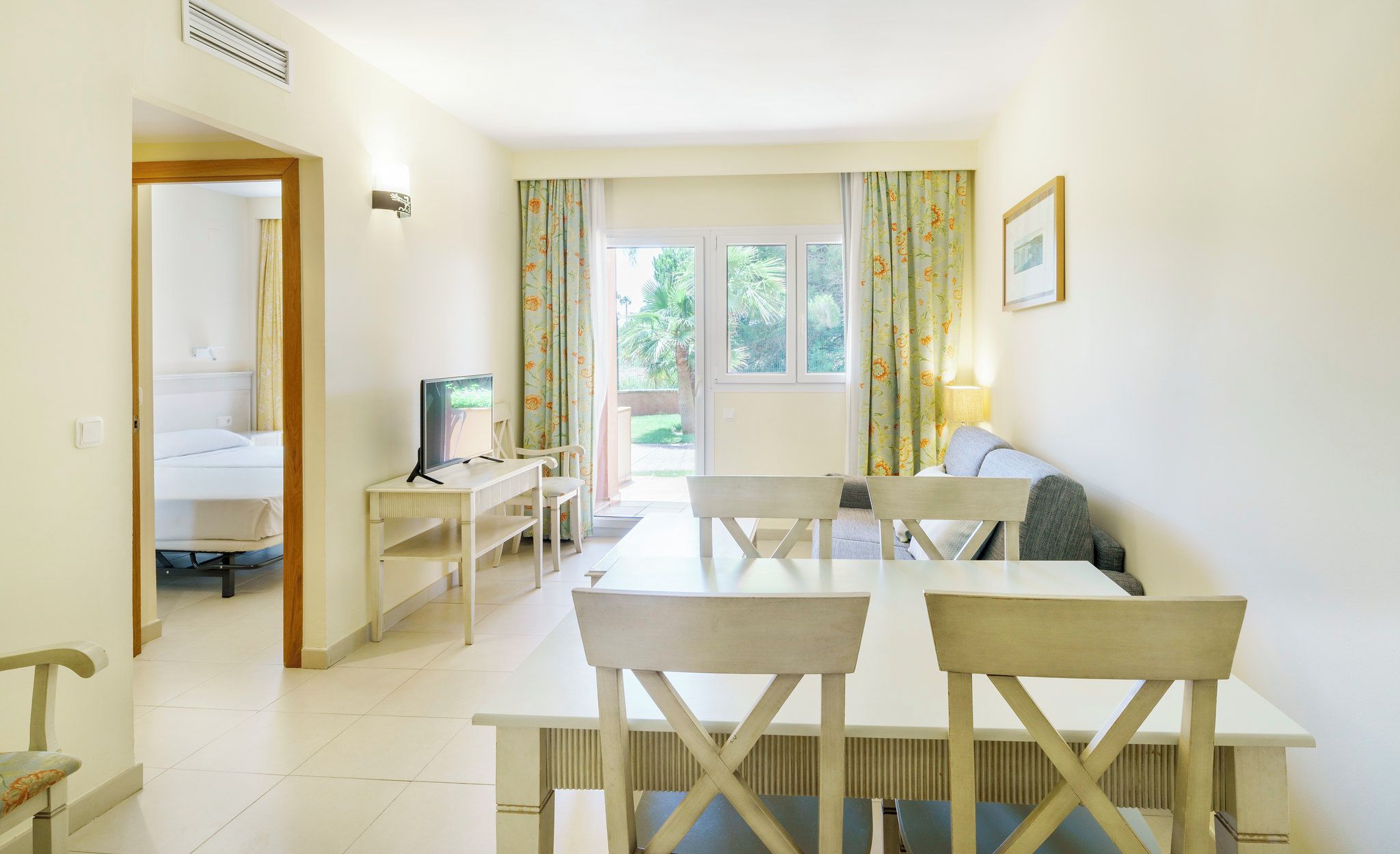 Una habitación con una mesa de comedor, sillas, un televisor, un sofá y una ventana con cortinas.