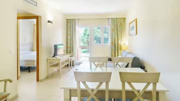 Una habitación con una mesa de comedor, sillas, un televisor, un sofá y una ventana con cortinas.