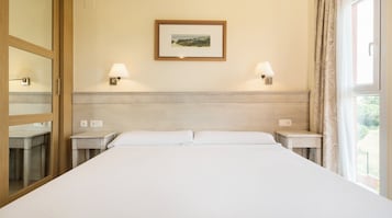 Una camera d'albergo con un letto grande, due lampade ai comodini, un quadro appeso al muro e una finestra con tende.